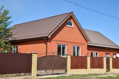 Brown roof on a red brick house that's situated behind a gate and fence