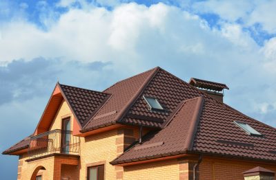 Red tile roof on a light brown house against a blue sky with clouds